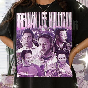 May include: Black t-shirt with a purple graphic featuring the text "BRENNAN LEE MULLIGAN" and several images of a man. The design has a vintage, distressed appearance, with a purple and white colour scheme.