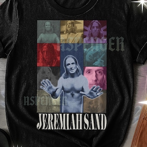 May include: Black unisex t-shirt with a multi-panel design. The central image is of a man with outstretched arms, surrounded by other images of the same man. The text "JEREMIAH SAND" is in a stylized font. The shirt also has the text "UNISEX TSHIRT".