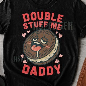 May include: Black unisex t-shirt with a graphic of a cartoon cookie with a tongue sticking out. The text on the shirt reads "DOUBLE STUFF ME DADDY" in red letters. Pink hearts surround the cookie.