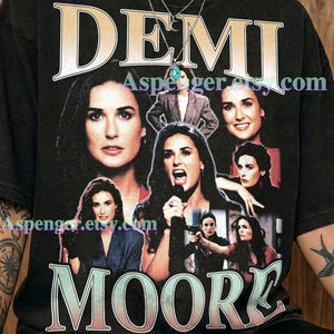 May include: A graphite-colored t-shirt featuring a collage of Demi Moore photographs. The name DEMI MOORE is printed in large, stylized lettering at the top and bottom. The shirt includes the text Aspenger.etsy.com and Comfort Colors : Graphite.