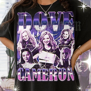 May include: Black t-shirt featuring a graphic design with the name "DOVE CAMERON" in purple and white text. The design includes multiple images of a woman with long wavy hair, with a purple and white lightning bolt design.
