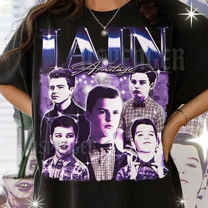 May include: Black graphic t-shirt featuring a purple and white design with the name "IAIN Armitage" and multiple images of the actor. The design has a vintage, distressed look.