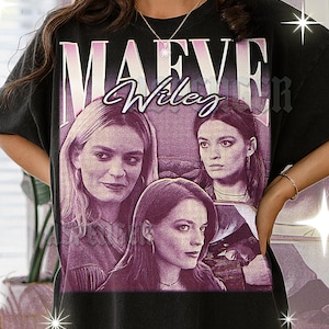 Puede incluir: Camiseta negra con un gráfico de estilo vintage de tres mujeres y el texto "MAEVE Wiley" en morado y blanco. El diseño tiene un aspecto descolorido y desgastado.