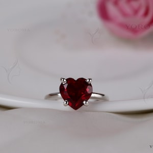 Puede incluir: Un anillo de plata con una piedra preciosa de color rojo intenso en forma de coraz&oacute;n, sujeta por un engaste de cuatro garras. La banda es lisa y met&aacute;lica, con un acabado pulido. El dise&ntilde;o se centra en la piedra roja facetada visible.