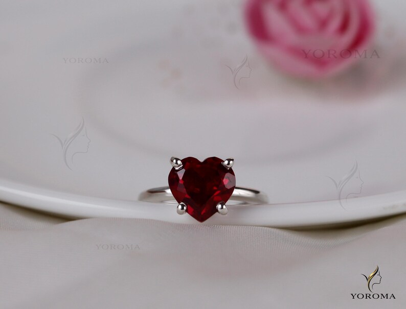 Puede incluir: Un anillo de plata con una piedra preciosa de color rojo intenso en forma de coraz&oacute;n, sujeta por un engaste de cuatro garras. La banda es lisa y met&aacute;lica, con un acabado pulido. El dise&ntilde;o se centra en la piedra roja facetada visible.