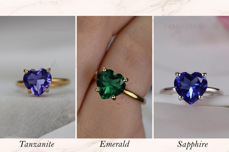 Puede incluir: Tres anillos con piedras preciosas en forma de coraz&oacute;n etiquetados como YOROMA. El primero es una tanzanita morada en banda dorada, el segundo una esmeralda verde en banda dorada y el tercero un zafiro azul en banda plateada, cada uno con cuatro garras.