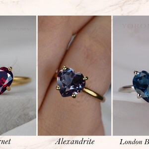 Puede incluir: Tres anillos con piedras preciosas talladas en forma de coraz&oacute;n. El primero es un granate rojo en banda dorada. El segundo es una alejandrita en banda dorada. El tercero es un topacio azul de Londres en banda plateada. Cada uno dice YOROMA.