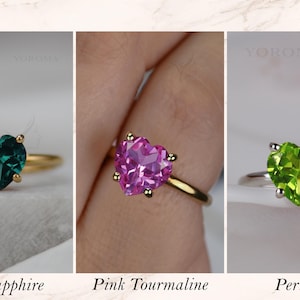 Puede incluir: Tres anillos con piedras preciosas talladas en forma de coraz&oacute;n. El primero es un zafiro azul verdoso en banda dorada, el segundo una turmalina rosa en banda dorada y el tercero un peridoto verde brillante en banda plateada, con sus nombres.