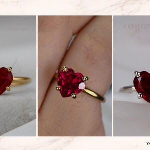 Puede incluir: Un anillo con una piedra preciosa roja en forma de coraz&oacute;n, tallada con facetas y montada en un engaste de cuatro garras. El anillo est&aacute; disponible en bandas de metal dorado y plateado. La marca YOROMA aparece en las esquinas de la imagen.