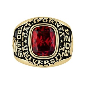 May include: A gold-toned ring featuring a large, rectangular, faceted deep red stone in the center. The black enamel border is inscribed with the text CALIFORNIA UNIVERSITY, TROJANS, and the year 2024, with gold relief details on the sides.