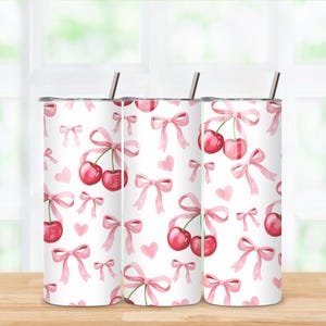 May include: White tumbler featuring a pattern of watercolor cherries, pink bows, and hearts. The tumbler has a silver lid and a silver straw. The design is feminine and whimsical, suitable for a gift.