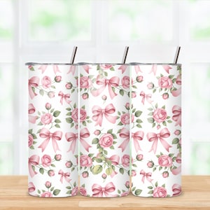May include: Three white insulated tumblers with a repeating pattern of pink roses and bows. Each tumbler has a silver-colored lid and a silver straw. The floral design includes green leaves.