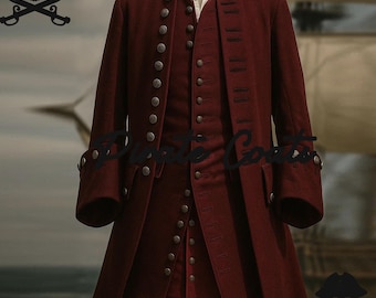 May include: A burgundy pirate coat and vest set with multiple silver buttons. The coat has long sleeves and a long, tailored fit. The vest is buttoned up and worn under the coat. The outfit is displayed on a mannequin. The background includes a pirate ship.