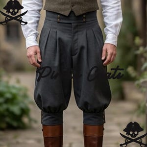 Op de afbeelding: Donkergrijze, hoog getailleerde broek met plooien en knoopdetails. De broek wordt gecombineerd met bruine laarzen en een vest. De afbeelding bevat de tekst "Purr Cats" en een piraten schedel logo.