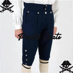 Op de afbeelding: Marineblauwe piratenbroek met zilveren knopen. De broek heeft een hoge taille en is knielang. De tekst "Pirate Coats" is zichtbaar op de broek. Het model draagt witte sokken met zwarte banden.