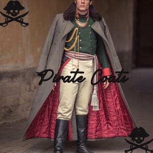 Puede incluir: Un abrigo largo gris con forro acolchado rojo, usado sobre una chaqueta verde y pantalones color crema. El abrigo tiene un cuello de piel y detalles dorados. La imagen incluye el texto "Pirate Coats" y un logotipo de pirata con calavera y espadas cruzadas.