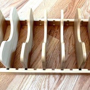 May include: A wooden knife block with slots for storing knives. The block is made of light-colored wood and has a rectangular base with vertical dividers. The knife slots are designed to hold various sizes of knives.
