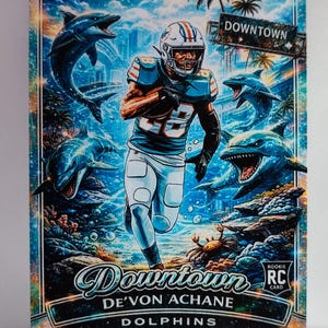 May include: A football trading card featuring a player in a teal and white uniform, running through a stylized underwater scene with dolphins. The card has the text "Downtown" and "De'Von Achane Dolphins".