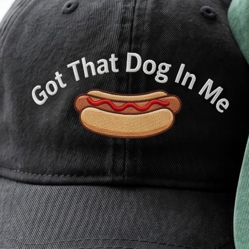 Puede incluir: Gorra de b&eacute;isbol negra con la frase bordada "Got That Dog In Me" sobre un dibujo de un perrito caliente con salsa roja. La gorra est&aacute; hecha de una tela suave y duradera.