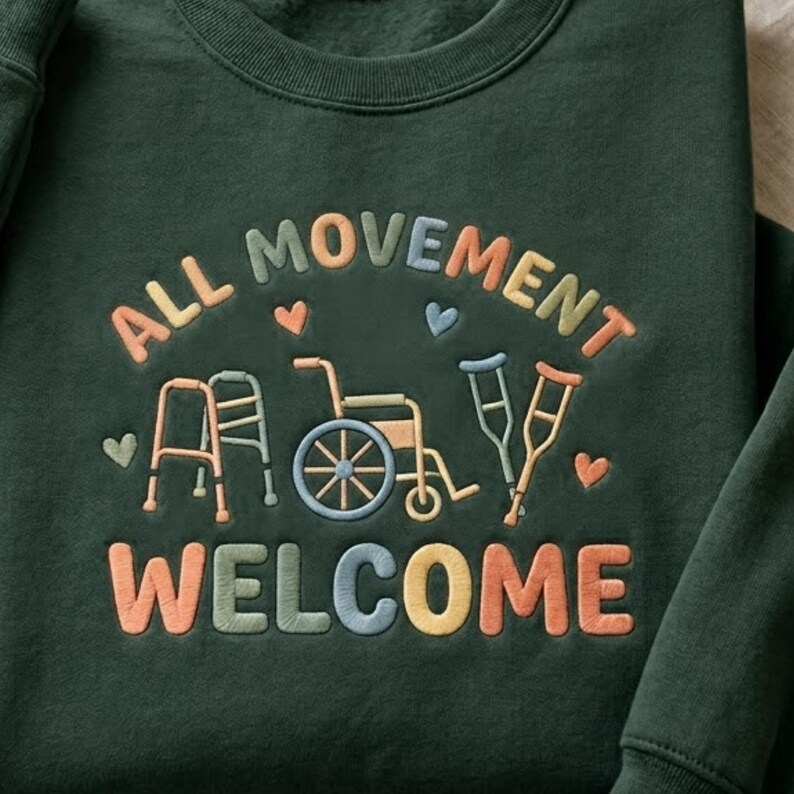 May include: Dark green sweatshirt with embroidered text and graphics. The text reads "ALL MOVEMENT WELCOME" in colorful letters. Graphics include a walker, wheelchair, and crutches, with heart accents.