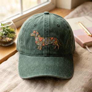 May include: A green baseball cap featuring an embroidered dachshund design filled with colorful flowers. The cap is made of a soft, textured fabric and has a curved brim. The hat is a stylish accessory for dog lovers.