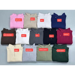 Peut inclure: Une collection de sweat-shirts &agrave; quart de fermeture &eacute;clair pli&eacute;s, de couleurs vari&eacute;es : rose clair, sable, cendre, marine, chocolat noir, bordeaux, blanc, gris, noir, beige, gris sport, vert militaire et vert for&ecirc;t. Chaque sweat a une &eacute;tiquette de couleur.
