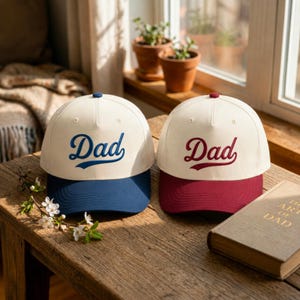 Op de afbeelding: Twee baseballpetten met off-white kronen en gestructureerde panelen. De linkerpet heeft een blauwe klep en het woord Dad geborduurd in blauw schrift. De rechterpet heeft een bordeauxrode klep en het woord Dad geborduurd in bordeauxrood schrift.