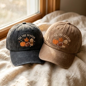 Peut inclure: Deux casquettes de baseball, une gris anthracite et une marron, arborant chacune une broderie représentant une citrouille, un ballon de football, une feuille d'érable et un café avec le texte 'TIS THE SEASON' inscrit en lettres blanches.