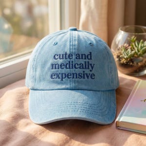 Könnte beinhalten: Hellblaue Baseballkappe mit dem gestickten Text "cute and medically expensive". Die Kappe hat einen gebogenen Schirm und eine runde Oberseite. Der Hut ist aus einem weichen, denimartigen Material.