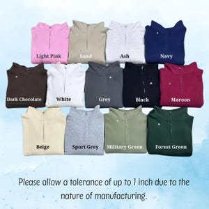 May include: A collection of quarter-zip pullovers in various colors, including light pink, sand, ash, navy, dark chocolate, white, grey, black, maroon, beige, sport grey, military green, and forest green. The text on the image says "Please allow a tolerance of up to 1 inch due to the nature of manufacturing."