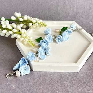 May include: A delicate blue flower bracelet with pearl accents. The bracelet is made of faux flowers and is strung on a silver chain.