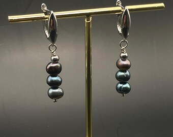 May include: A pair of silver hoop earrings with three black pearls dangling from each hoop.