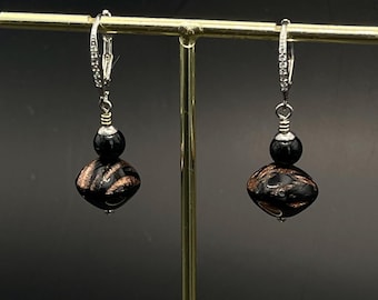 May include: A pair of black and gold dangle earrings with a silver hoop and a black bead. The earrings feature a black and gold patterned bead.