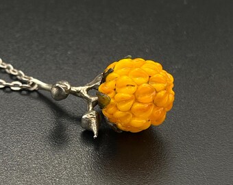 Op de afbeelding: Een zilveren ketting met een gele glazen bessen hanger. De bes heeft een getextureerd oppervlak en een zilveren steel.