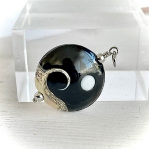Peut inclure: Pendentif en verre noir et blanc avec un motif yin yang. Le pendentif a une bélière argentée et une perle argentée.