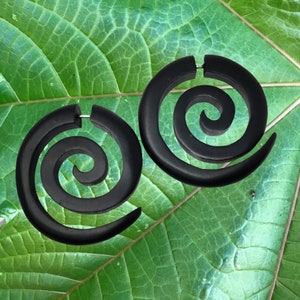 May include: A pair of black wooden spiral earrings. The earrings are large and have a simple design.