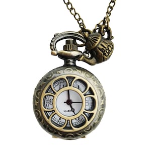 May include: A gold-toned pocket watch with a white face and black hands. The watch has a decorative design around the edge and is attached to a chain with a teapot charm.