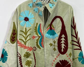 May include: A light green jacket with colorful floral embroidery. The jacket features turquoise, red, and green embroidered flowers and leaf designs. The jacket is hanging on a wooden hanger.