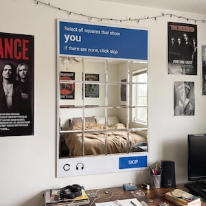 May include: A large mirror with a grid pattern, resembling a webpage element, hangs on a white wall. The mirror reflects a bedroom scene. Above the mirror, text reads "Select all squares that show you. If there are none, click skip."