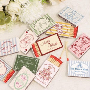 Op de afbeelding: Een verzameling decoratieve lucifersdoosjes met diverse ontwerpen en teksten, waaronder namen en data. De doosjes tonen verschillende kleurenschema's en illustraties, perfect voor huwelijksbedankjes of speciale evenementen.