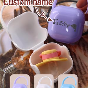 May include: A collection of baby pacifier cases in various colors, including white, lavender, and blue. The cases have a handle and a snap closure. One case is open, revealing a pacifier. The text "Custom name" is visible, along with the name "Felicity" on one case.