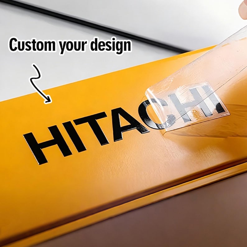 May include: A yellow surface featuring the black text HITACHI being applied with a clear transfer film. The image includes the text Custom your design with a curved arrow pointing toward the lettering, demonstrating a custom decal application process.