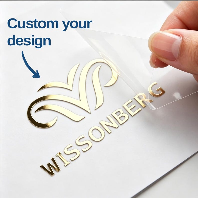 May include: A gold metallic decal featuring a stylized emblem and the text WISSONBERG, partially peeled from a clear transfer sheet. The text Custom your design is printed in blue with a blue arrow pointing toward the gold emblem.