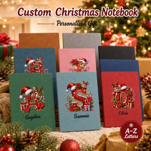 May include: A collection of rectangular notebooks in various colors including green, blue, pink, and red. Each notebook features a large, decorative letter adorned with a reindeer, Santa hat, and poinsettias. Some covers display names like Angelica, Sammie, and Olivia.