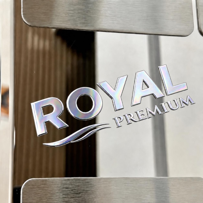May include: A polished stainless steel surface featuring the embossed text ROYAL PREMIUM in a metallic, reflective finish. The letters have a slight iridescent sheen, and a stylized swoosh graphic is positioned directly beneath the word ROYAL.