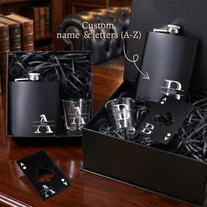 May include: A black gift set containing a matte black metal flask, a clear glass shot glass, and a black metal bottle opener shaped like an ace of spades playing card. The items feature white custom lettering and monograms including Alex and Belle.