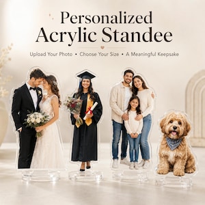 Puede incluir: Cuatro expositores de acrílico personalizados con impresiones fotográficas. Los expositores muestran a una pareja de novios, una graduada con toga, una familia de tres personas y un perro peludo con pañuelo azul, sobre bases circulares.