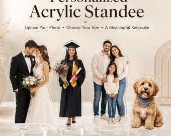 May include: Four personalized acrylic standees featuring custom photo prints. The standees display a wedding couple, a graduate in a cap and gown, a family of three, and a fluffy dog wearing a blue bandana, all mounted on clear circular bases.