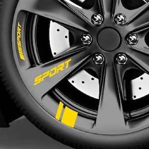 Puede incluir: Una llanta de coche negro mate con calcomanías de vinilo de color amarillo brillante. El diseño incluye la palabra SPORT en una fuente sans-serif en negrita, junto con rayas amarillas verticales aplicadas en los radios y el borde exterior.