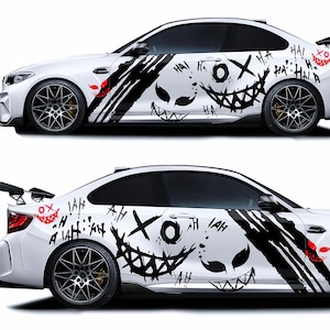 Può includere: Auto bianca con decalcomanie grafiche nere e rosse. Le decalcomanie presentano una faccia sorridente, la parola "HA!" e altri simboli. L'auto ha cerchi neri e uno spoiler.